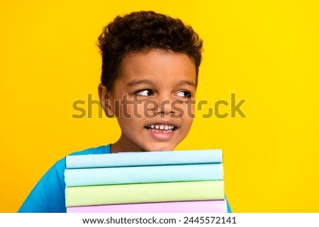 Portrait of multiethnic multinational boy wear blue stylish t-shirt hold book look at sale empty space isolated on vivid yellow background Royalty-Free Stock Photo #2445572141