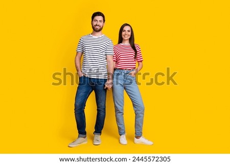 Full size photo of two people girl guy dressed striped t-shirt hold hands together arms in pockets isolated on yellow color background
