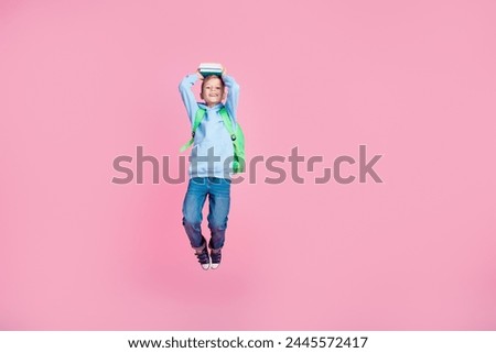 Full size portrait of cheerful schoolchild jump hold book above head empty space ad isolated on pink color background