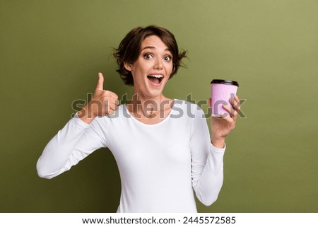Photo portrait of attractive young woman hold paper cup enjoy show thumb up wear trendy white clothes isolated on khaki color background