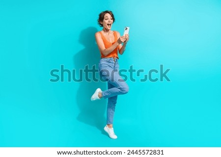 Full size photo of ecstatic nice girl dressed knitwear top denim pants astonished staring at smartphone isolated on blue color background