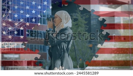 Image of American flag waving with jigsaw puzzles revealing biracial woman in hijab taking photos with camera in the background. American society diversity concept digital composition.