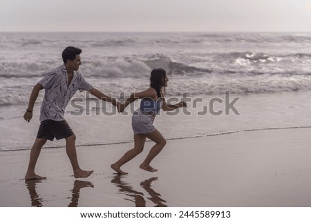 Couple running hand in hand along the seashore in the afternoon, getting their feet wet.