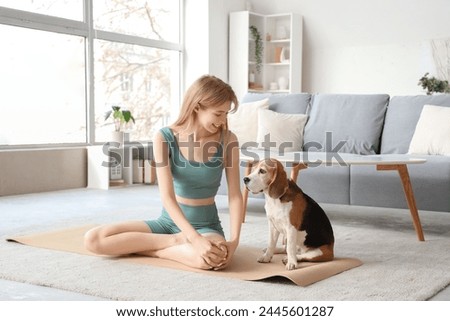 Sporty young woman with Beagle dog sitting on yoga mat at home Royalty-Free Stock Photo #2445601287