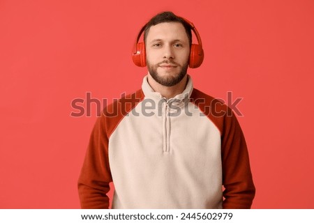 Young man in modern headphones on red background