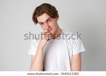 Smiling Young Man in White T-Shirt Posing With Hand on Chin Against a Gray Background