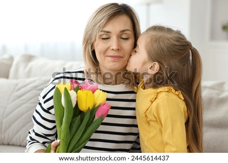Little daughter kissing and congratulating her mom with Mother`s Day at home. Woman holding bouquet of beautiful tulips