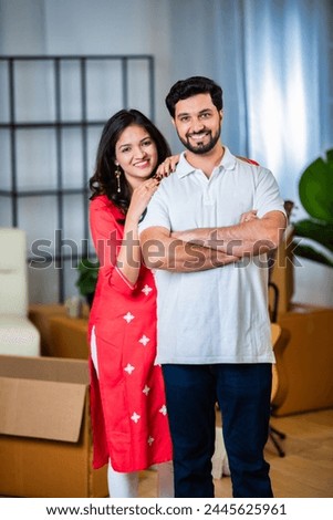 Indian young couple standing together in new house and looking at camera with smile