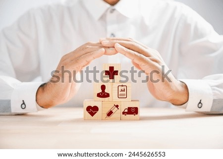 Wooden cube block displaying healthcare icons, topped by a doctor hand indicating protection, exemplifying healthcare and insurance concept. Building a secure medical future. Health care concept
