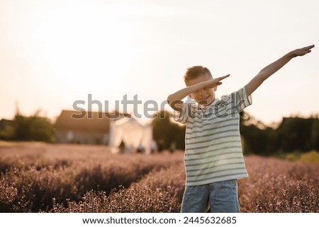 Happy young american guy performing show dance on summer day at sunset. Cheerful child presenting popular internet meme pose in lavender field. Boy making dab move gesture, having fun. Sneeze gesture.