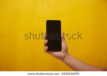 Hand holding a smartphone on yellow background 