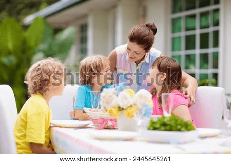 Family eating outdoors. Garden summer or spring fun. Barbecue in sunny backyard. Mother’s day or Easter celebration. Kids eat lunch in outdoor deck in pastel colors. Parents and children enjoy bbq.  Royalty-Free Stock Photo #2445645261