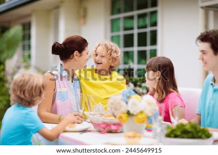 Family eating outdoors. Garden summer or spring fun. Barbecue in sunny backyard. Mother’s day or Easter celebration. Kids eat lunch in outdoor deck in pastel colors. Parents and children enjoy bbq. 