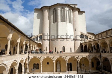 Pilgrims and tourists are visiting the Friary of St. Francis next to the Basilica of San Francesco d'Assisi in Assisi, Italy. It was built with pink and white stone from Mount Subasio.  Royalty-Free Stock Photo #2445654545