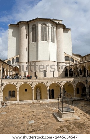 Pilgrims and tourists are visiting the Friary of St. Francis next to the Basilica of San Francesco d'Assisi in Assisi, Italy. It was built with pink and white stone from Mount Subasio.  Royalty-Free Stock Photo #2445654547