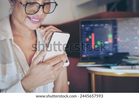 Happy woman feeling joy using cell phone and money bill in living room.Cryptocurrency investor trading at home.Concept of money transfers, internet banking, online work, sports betting, passive income