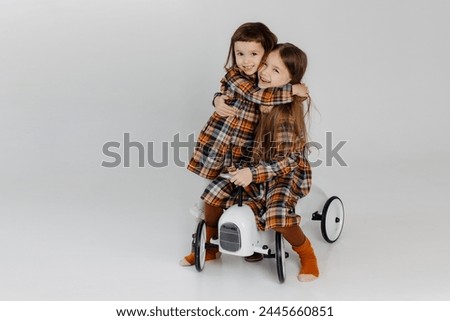 two little sisters, 6 and 3 years old, in stylish identical dresses, have fun and play on a studio cyclorama during a photo shoot