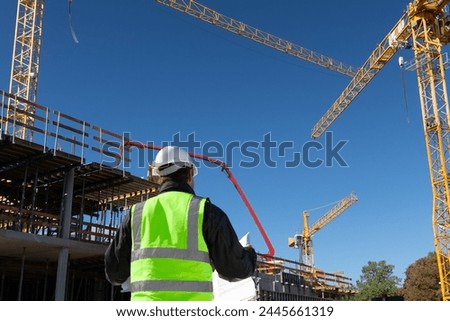 builder architect engineer foreman worker with hard hat and safety vest on major construction site with crane in background checking plan