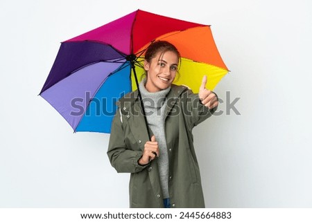 Young woman holding an umbrella isolated on white background with thumbs up because something good has happened