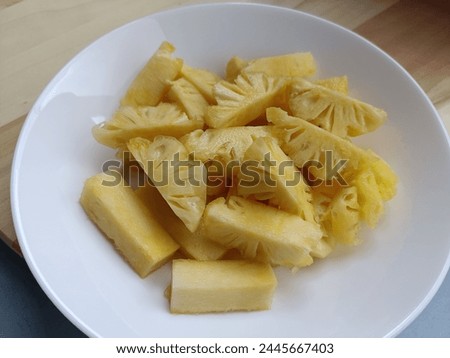 Phulae pineapple, sweet and fragrant taste. Cut into bite-sized pieces, both the meat and the core are Arranged in a white porcelain plate. It is a pineapple variety from Chiang Rai, Thailand. Royalty-Free Stock Photo #2445667403