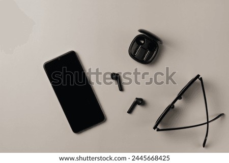 Black accessories on beige background. Phone, headphones, glasses