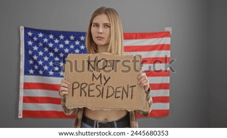 Caucasian blonde woman holds protest sign with american flag backdrop conveying political dissent