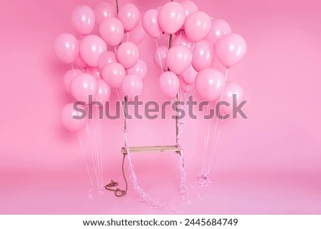 Romantic swing decorated with bunch of pink balloons on a pink background in the studio. Birthday and wedding celebration concept. Decor for holidays and events. Royalty-Free Stock Photo #2445684749