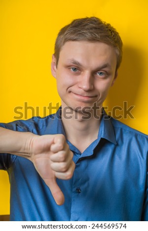 Handsome young man lowered his fist with the thumb down. gesture. Isolated yellow background. photo