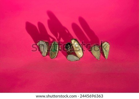 close-up of set of three silver rings with druses of natural multicolored minerals on a bright pink background with clear ring shadows