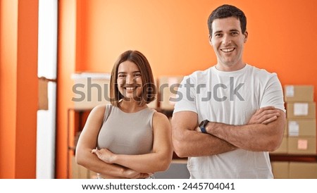 Two workers man and woman standing together with arms crossed gesture smiling at office
