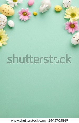 Easter elegance: pastels and florals in harmony. Top view vertical photo of decorated eggs, pink flowers and ceramic bunny on teal background with space for messages or promotions