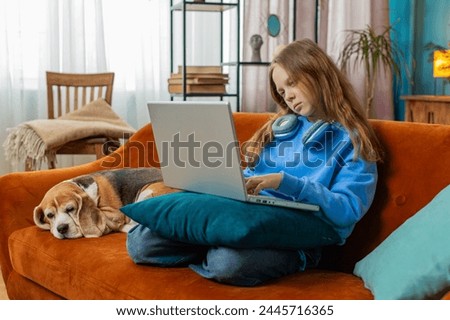 Overtired Caucasian girl bored using laptop while sitting on sofa near beagle dog. Sleepy teenage child cannot concentrate on work and types lazily. Female preteen is not interested in doing a project Royalty-Free Stock Photo #2445716365
