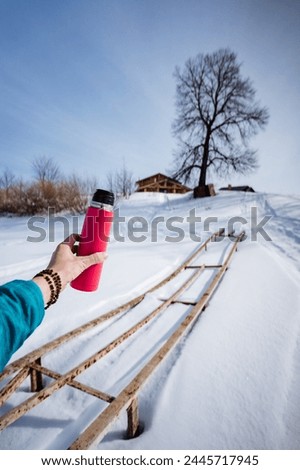 Pink thermos on tree background, winter trekking in the forest, hand holding thermos with hot drink, walk in spring park. High quality photo