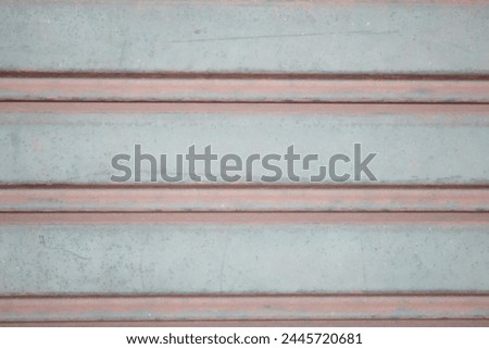 The metal wall, composed of riveted corrugated metal sheets, displays signs of rust and numerous holes. Additionally, graffiti adorns the surface.
