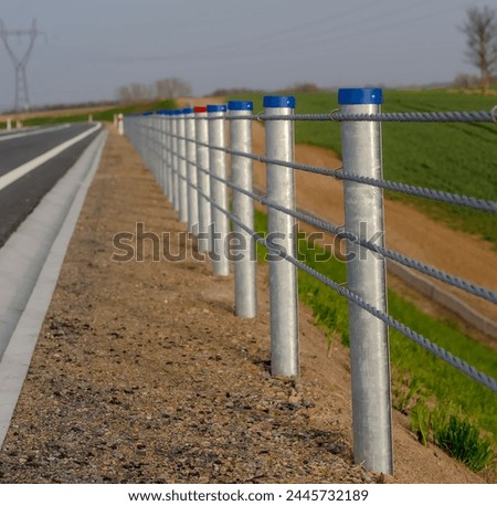 A handrail made of steel cables and posts on the edge of the road among fields in spring. Spring afternoon on the side of the road. Picturesque and handy, made of steel ropes, protecting the road .