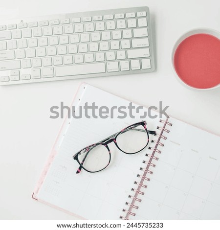 white workspace with light pink note book and white flower with coffee on white table background.