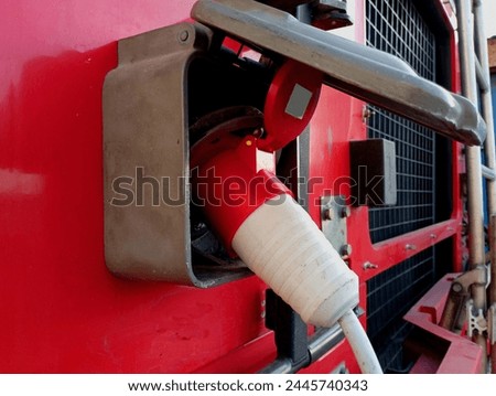 Charging electric batteries of a big red truck from the mains. The electric cable is inserted into the car socket.