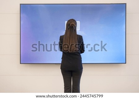 Professional woman in business attire standing in front of a huge blank monitor