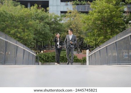 Two corporate employees in suits walk with purpose on a city bridge, discussing work