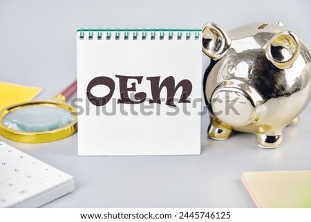 OEM original equipment manufacturer concept. Text on a white notebook on a gray background near a piggy bank, a calculator and stickers