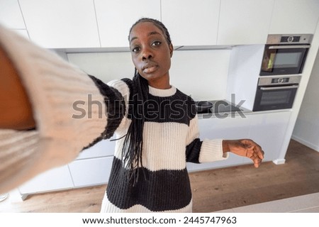 In this inviting image, a young woman extends her arm to take a selfie within the sleek confines of a modern kitchen. Her striped sweater adds a touch of personal style against the minimalist backdrop