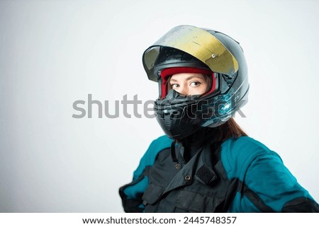 female motorcyclist in a helmet and motorcycle jacket against a white wall