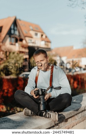 Man Sitting in Old European City And Holding Photo Camera. Contemporary Stylish Blogger And Photographer.