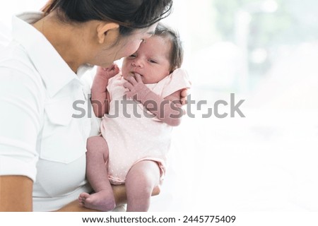 Mother carrying and kissing her newborn baby girl at home. Cute 19 days Asian Australian infant baby lean in mom arms. Parent and little kid relaxing at home. Family and child care concept