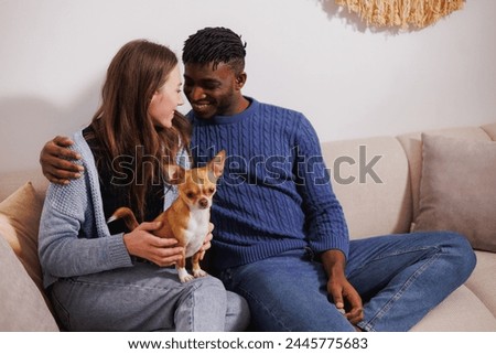 Smiling african american man hugging girlfriend with dog on couch at home
