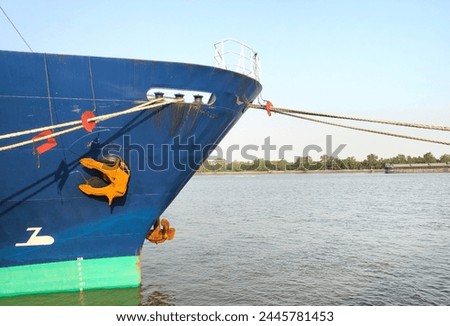 Anchor with large cargo ship's, anchor being pulled. Blue and green ship, While docked at the pier by large ropes on the river, in the background is a view of blue sky and transportation concept