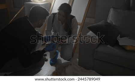 A man and woman investigate a crime scene indoors, examining evidence with gloves and flashlight.