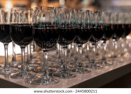 Wine glasses filled with red wine arranged and presented on a table top for self-service by party guests. Shallow depth-of-field image. A glass of red wine is on the table. Glasses of wine.  Royalty-Free Stock Photo #2445800211