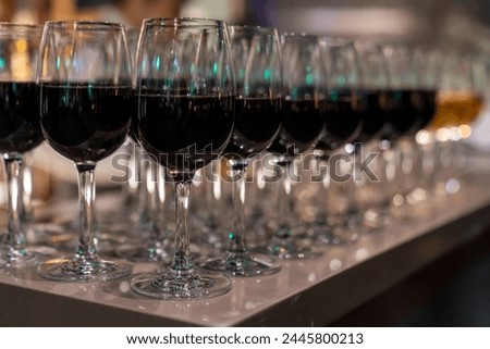 Wine glasses filled with red wine arranged and presented on a table top for self-service by party guests. Shallow depth-of-field image. A glass of red wine is on the table. Glasses of wine.  Royalty-Free Stock Photo #2445800213