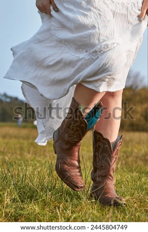 Woman in white dress modelling cowboy boots in a meadow during a sunset.
